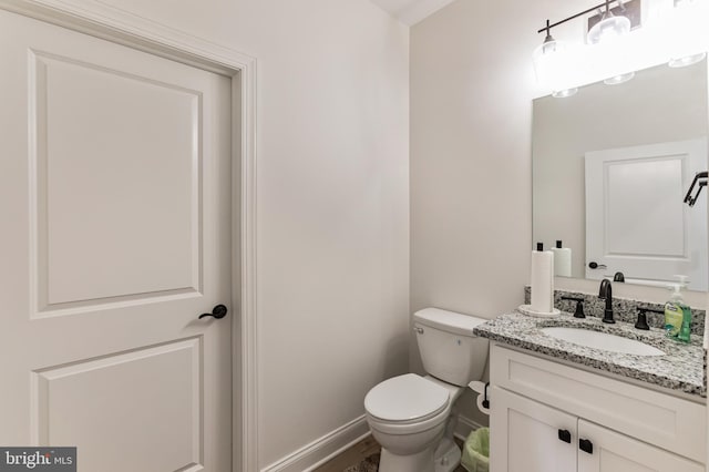 half bathroom with vanity, toilet, and baseboards