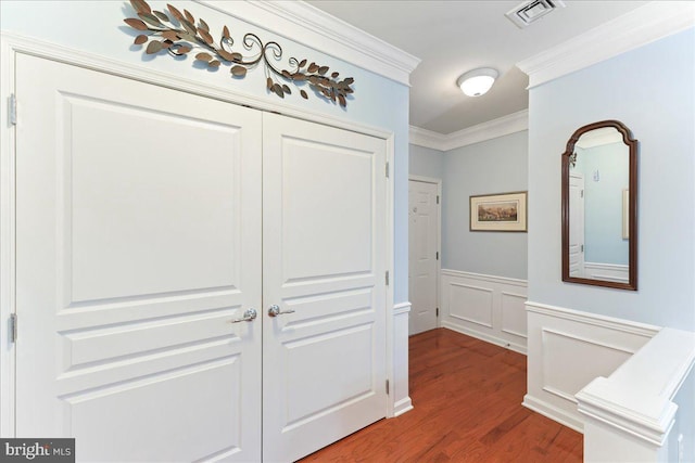 corridor with visible vents, crown molding, a wainscoted wall, wood finished floors, and a decorative wall