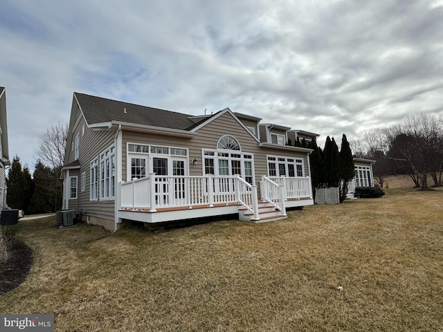 rear view of house with cooling unit, a lawn, a wooden deck, and a shingled roof