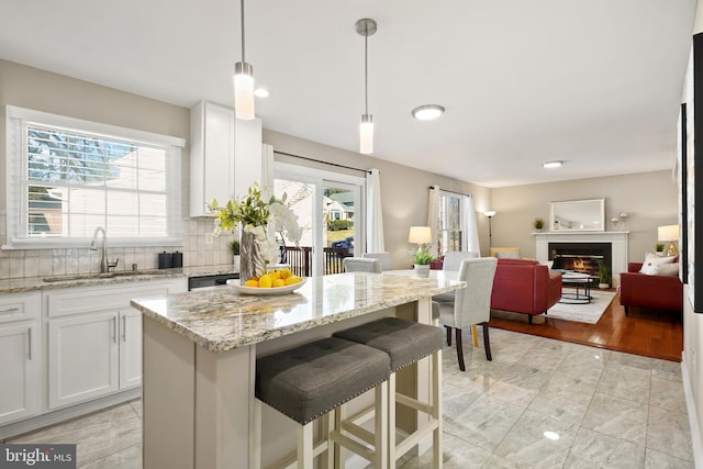 kitchen featuring open floor plan, decorative backsplash, a glass covered fireplace, white cabinets, and a sink