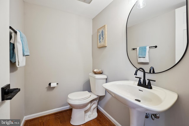 bathroom with toilet, wood finished floors, baseboards, and a sink