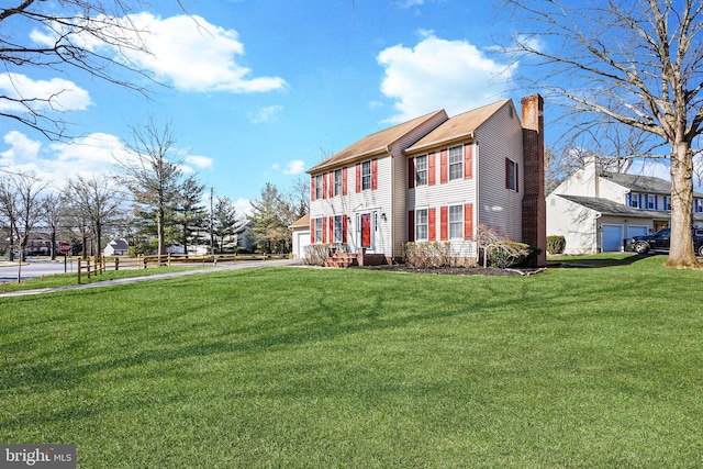 colonial home with a garage, driveway, a front yard, and a chimney