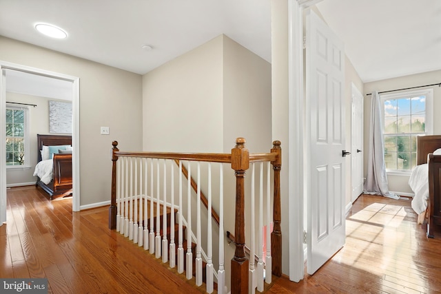 hallway with an upstairs landing, a healthy amount of sunlight, and hardwood / wood-style floors