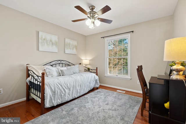 bedroom with ceiling fan, visible vents, baseboards, and wood finished floors