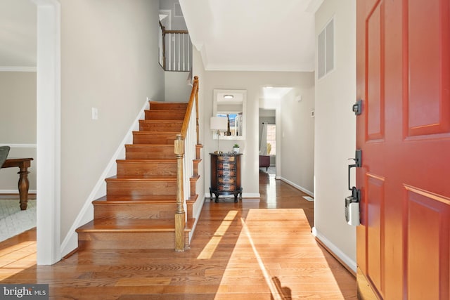 entryway featuring visible vents, crown molding, baseboards, stairs, and wood finished floors