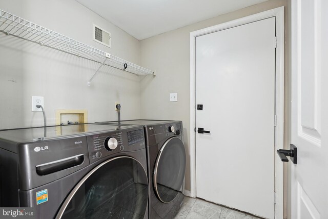 clothes washing area with laundry area, visible vents, and washing machine and clothes dryer