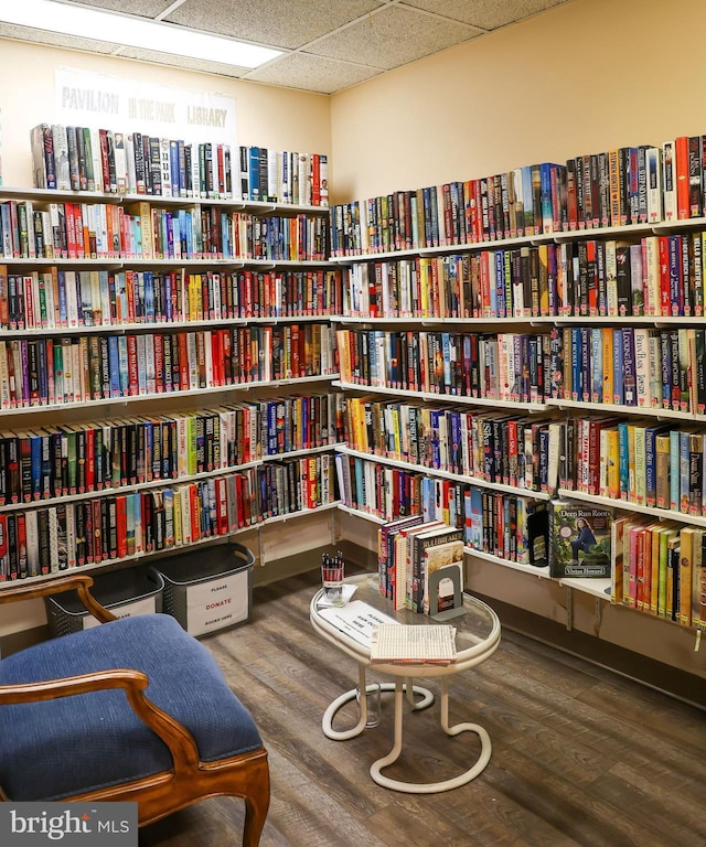 living area featuring wall of books, wood finished floors, and a paneled ceiling