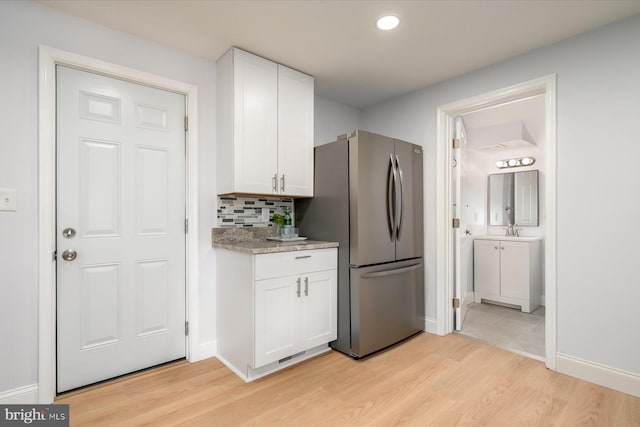 kitchen featuring light wood-style floors, freestanding refrigerator, white cabinets, and backsplash