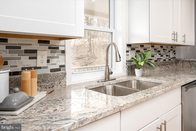 kitchen with light stone counters, a sink, white cabinetry, stainless steel dishwasher, and tasteful backsplash