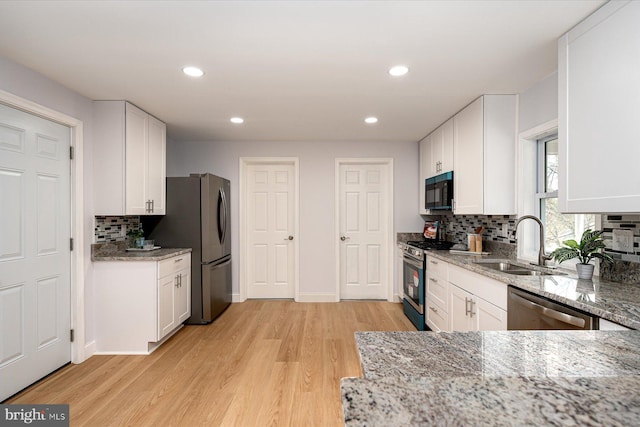 kitchen featuring stainless steel appliances, white cabinetry, a sink, and light stone countertops