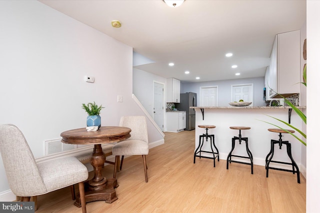 kitchen with light wood finished floors, white cabinets, a breakfast bar area, freestanding refrigerator, and a peninsula