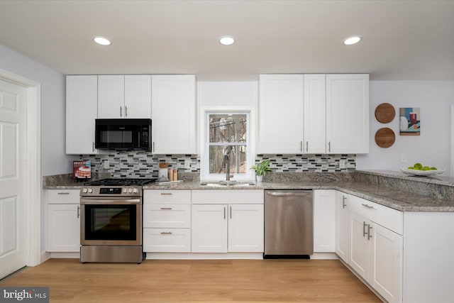 kitchen featuring white cabinets, a peninsula, stainless steel appliances, light wood-style floors, and a sink