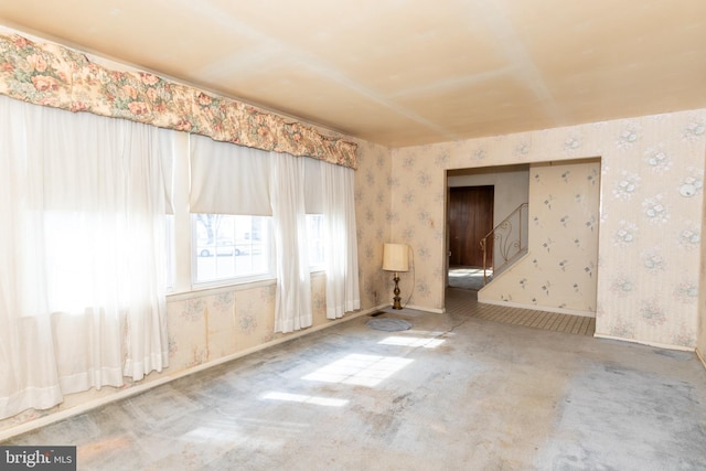 spare room featuring wallpapered walls, carpet, stairs, and baseboards