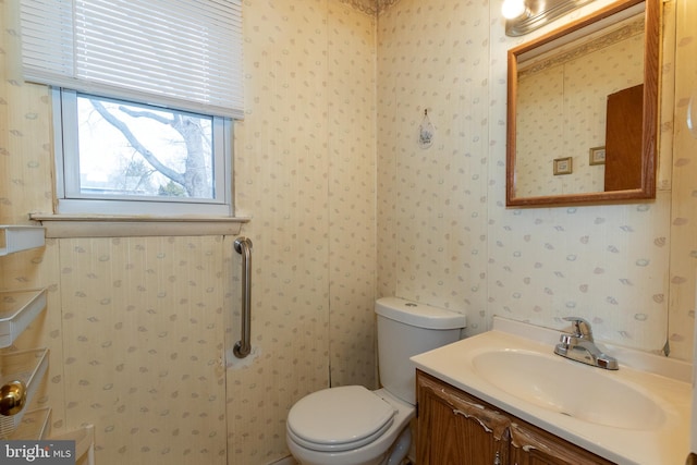 bathroom with vanity, toilet, and wallpapered walls