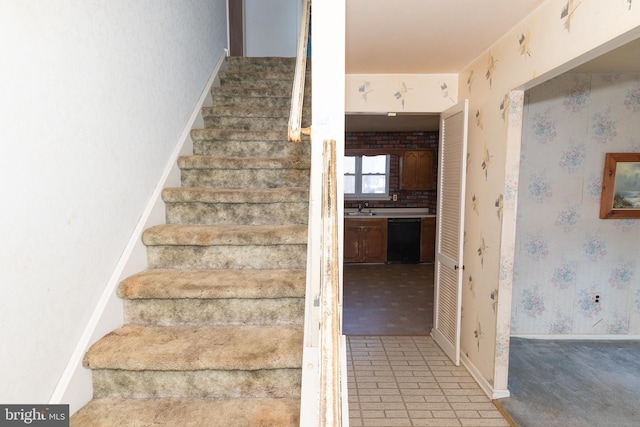 staircase with baseboards, brick floor, and wallpapered walls