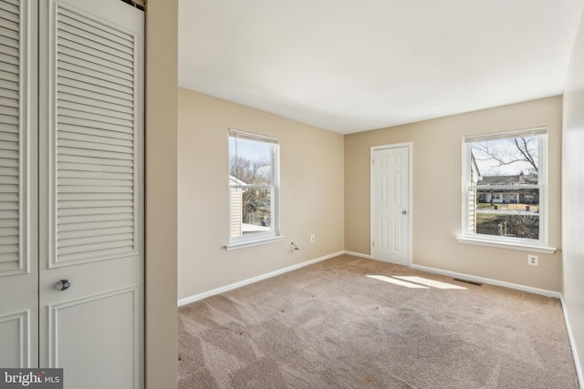 unfurnished bedroom featuring visible vents, multiple windows, carpet flooring, and baseboards