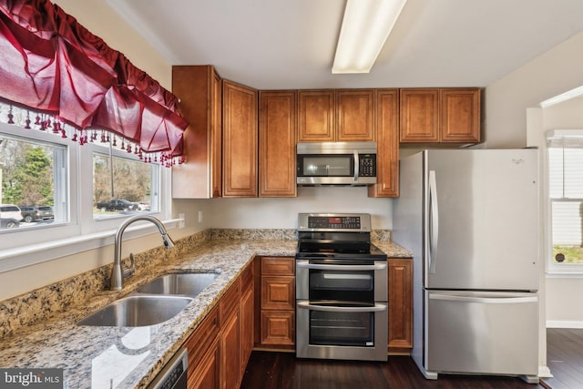 kitchen with brown cabinetry, stainless steel appliances, light stone counters, and a sink