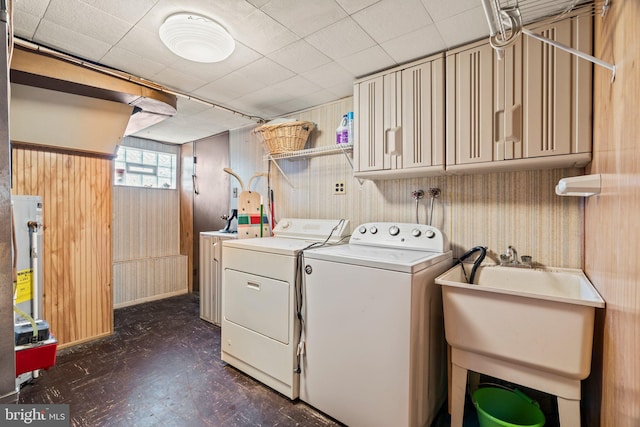 clothes washing area featuring a sink, gas water heater, wooden walls, and washing machine and dryer