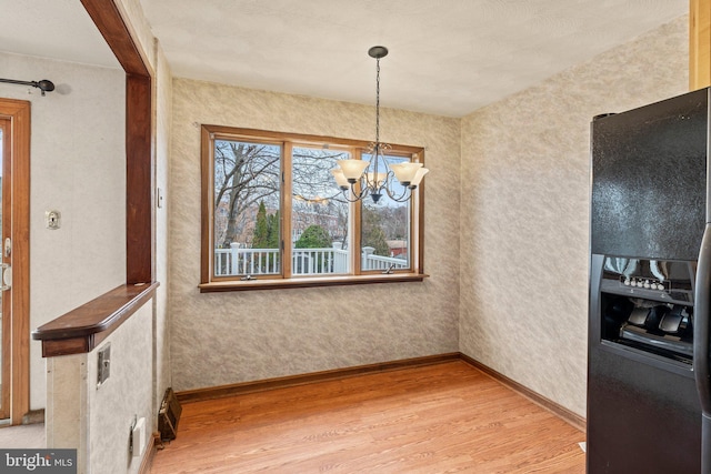 unfurnished dining area with a notable chandelier, light wood-style floors, and baseboards