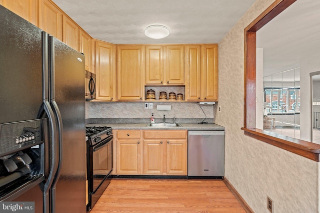 kitchen featuring light brown cabinets, light wood-type flooring, light countertops, black appliances, and a sink