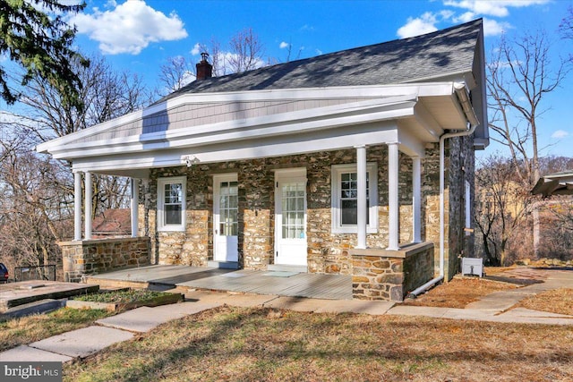 view of front of property with stone siding, a porch, and a shingled roof