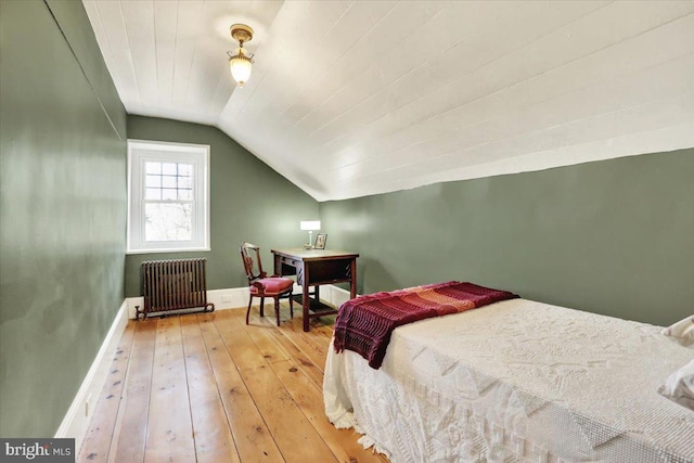 bedroom with hardwood / wood-style floors, vaulted ceiling, radiator, and baseboards