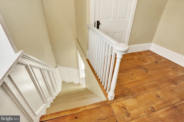 stairs with a decorative wall, wainscoting, and wood finished floors