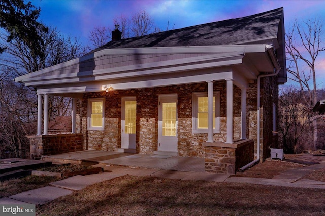 view of front facade with stone siding, a porch, and a shingled roof