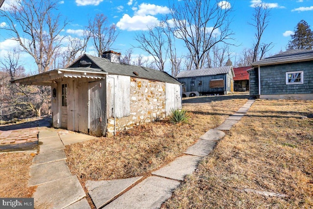 view of property exterior with a chimney, an outdoor structure, and a shingled roof