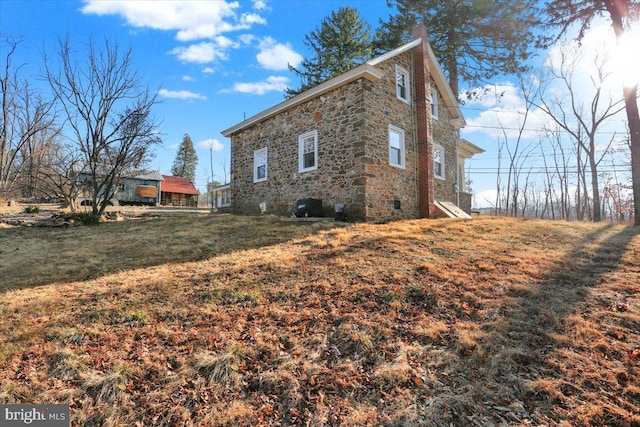 view of property exterior featuring stone siding, a chimney, and a yard