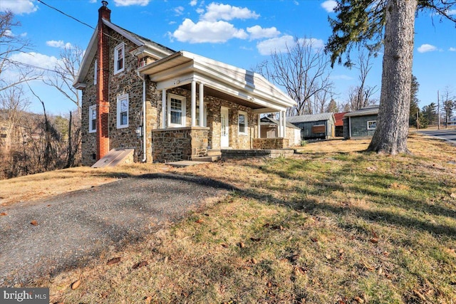 view of front of property featuring a front yard, covered porch, stone siding, and a chimney