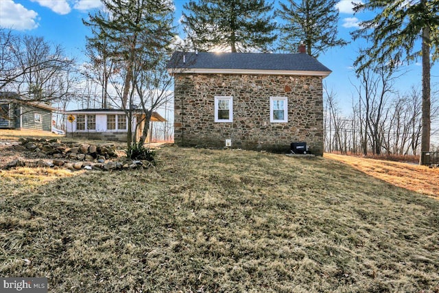 view of home's exterior featuring stone siding, a lawn, and a chimney