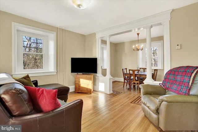 living room featuring a chandelier, light wood-style flooring, baseboards, and ornate columns