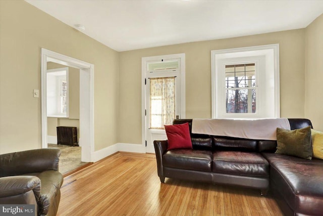 living area with baseboards, a healthy amount of sunlight, radiator heating unit, and hardwood / wood-style flooring