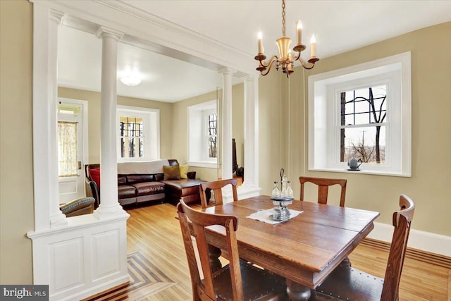 dining space featuring a healthy amount of sunlight, an inviting chandelier, light wood-type flooring, and ornate columns