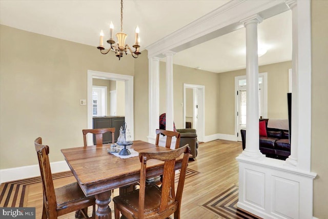 dining room with decorative columns, baseboards, a chandelier, and light wood finished floors