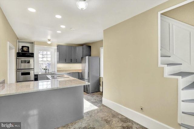 kitchen with light stone countertops, appliances with stainless steel finishes, a peninsula, and gray cabinets