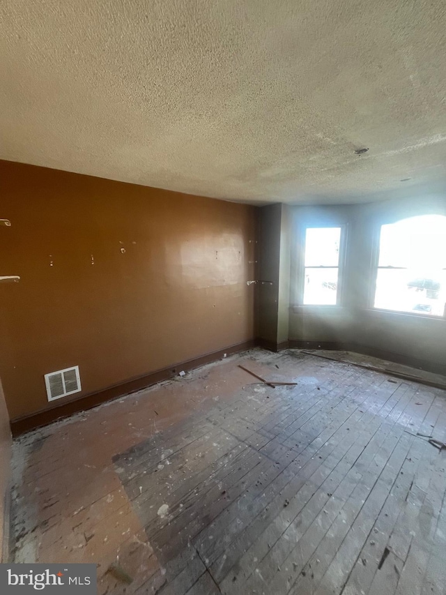 empty room featuring visible vents, a textured ceiling, baseboards, and hardwood / wood-style flooring