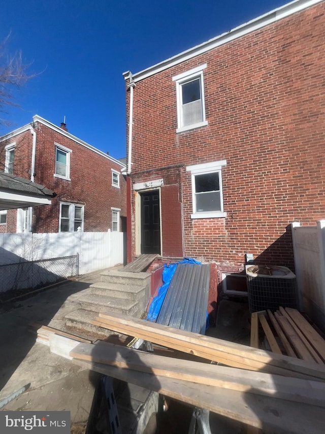 back of house with brick siding, fence, and central AC