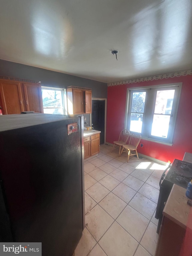 kitchen featuring light tile patterned floors, plenty of natural light, brown cabinetry, and freestanding refrigerator