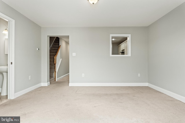 carpeted spare room featuring stairway and baseboards