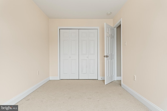 unfurnished bedroom featuring a closet, light colored carpet, and baseboards