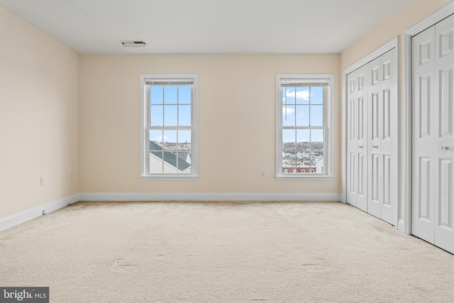 unfurnished bedroom with baseboards, carpet, visible vents, and multiple closets