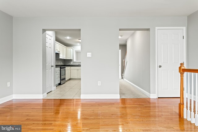 empty room featuring light wood-style floors, stairway, and baseboards