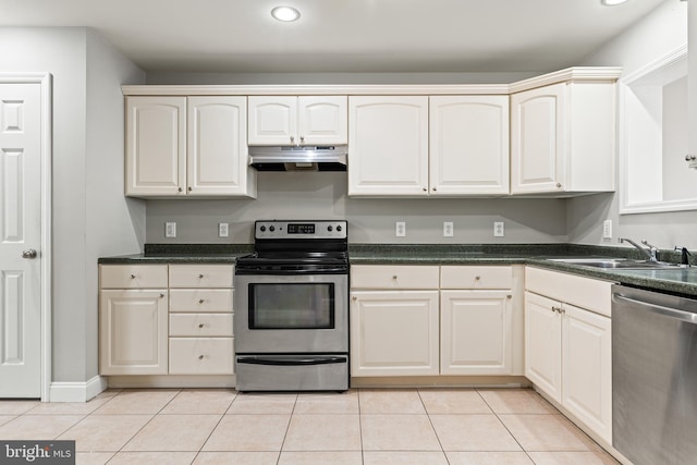 kitchen with light tile patterned flooring, under cabinet range hood, a sink, appliances with stainless steel finishes, and dark countertops