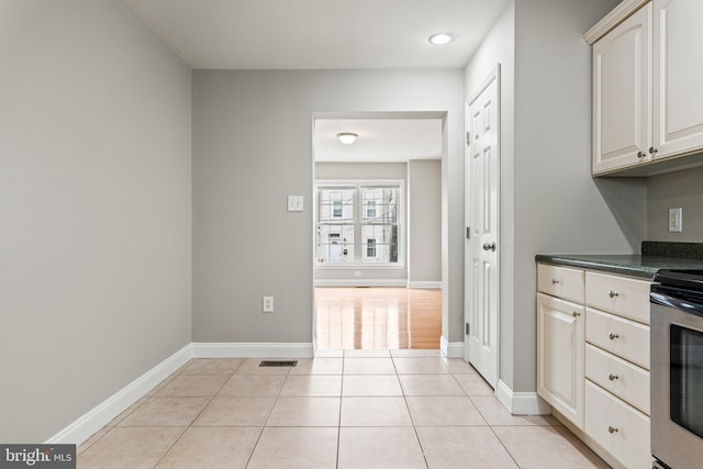 kitchen featuring stainless steel electric stove, light tile patterned floors, dark countertops, visible vents, and baseboards