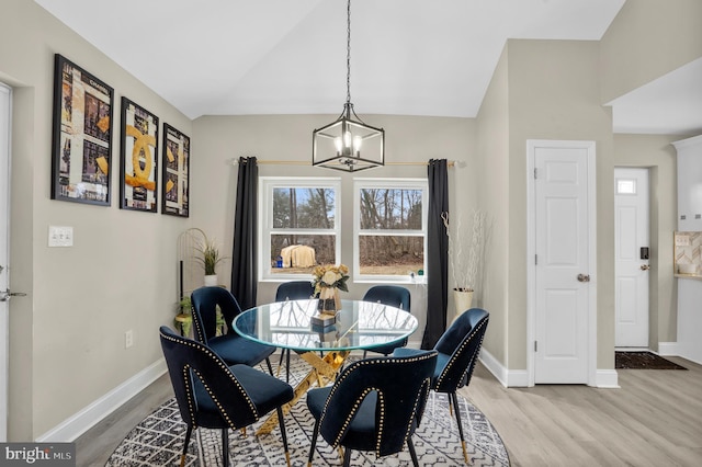 dining space with an inviting chandelier, light wood-style flooring, baseboards, and vaulted ceiling