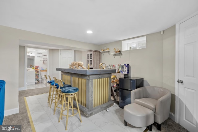 bar featuring baseboards, freestanding refrigerator, marble finish floor, a bar, and recessed lighting