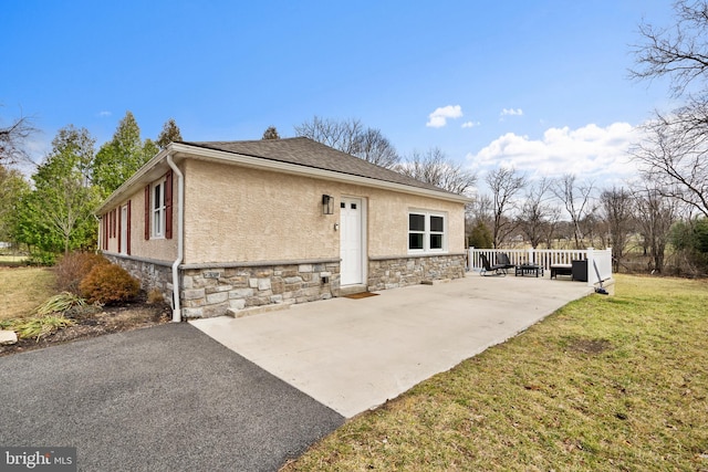 back of house with stone siding, a yard, a patio, and stucco siding