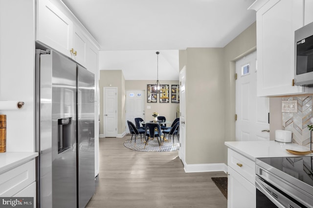 kitchen featuring appliances with stainless steel finishes, white cabinets, light wood-style floors, and decorative backsplash